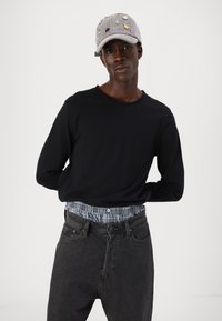 Căciulă gri cu diverse embellish-uri, cămașă neagră cu mânecă lungă și blugi gri cu un talie de tartan albastru.