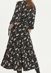 Svart klänning med trekvartsärmar och knytmidja, med ett mönster av rosa och vita fjädrar och en svängande kjol.