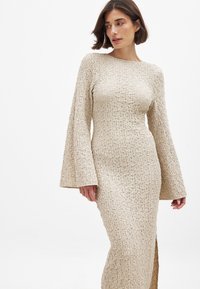 Pika-särk, sobiv beež kleit, mis on valmistatud tekstureeritud kangast, millel on sooneline muster, millel on tagasihoidlik paadi kaelus ja külgauk.