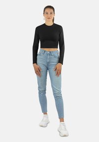 Schwarzes, langärmliges, cropped Oberteil, hochgeschnittene hellblaue Jeans und weiße Sneaker. Minimalistisches Design mit einer figurbetonten Silhouette.