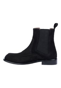 Stivale Chelsea in suede nero con pannelli elastici laterali, punta arrotondata e un passante sul retro. Suola piatta in cuoio con dettagli di cucitura minimi.