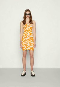 Vestido mini ajustado em padrões geométricos laranja e branco, com alças finas. Combinado com sapatos plataforma brancos chunky e óculos de sol pretos.