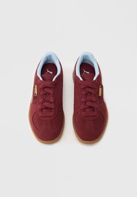 Červené sportovní boty z semiše se světle modrým límcem, šněrováním, zlatým logem a podrážkami z gumové pryže.