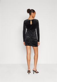 Rochie mini din catifea neagră cu mâneci lungi, texturată cu puncte mici, având o deschidere în formă de cheie la spate și detalii pliate pe lateral.