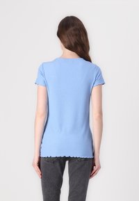 Tricou albastru cu dungi, cu mâneci scurte și tiv în formă de valuri, realizat dintr-un material elastic din bumbac, prezentat din spate.