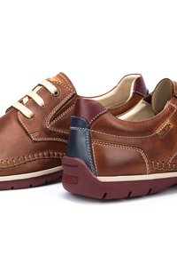 Zapatos de cuero marrón con un tacón azul marino contrastante, acentos en crema y cordones beige. Los detalles de costura en los laterales y la puntera realzan la textura.