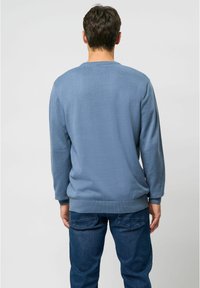 Blå strikket trøje med ribben ved håndleddene og i kanten, har en simpel rund halsudskæring og en struktureret mønster. Bæres med mørkeblå jeans.