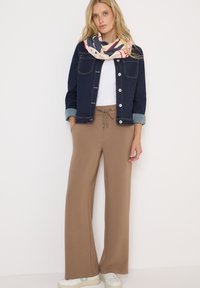 Pantaloni larghi marroni con cordoncino elastico, abbinati a una t-shirt bianca e a un giubbotto in denim scuro. Accessoriati con una sciarpa a fantasia.
