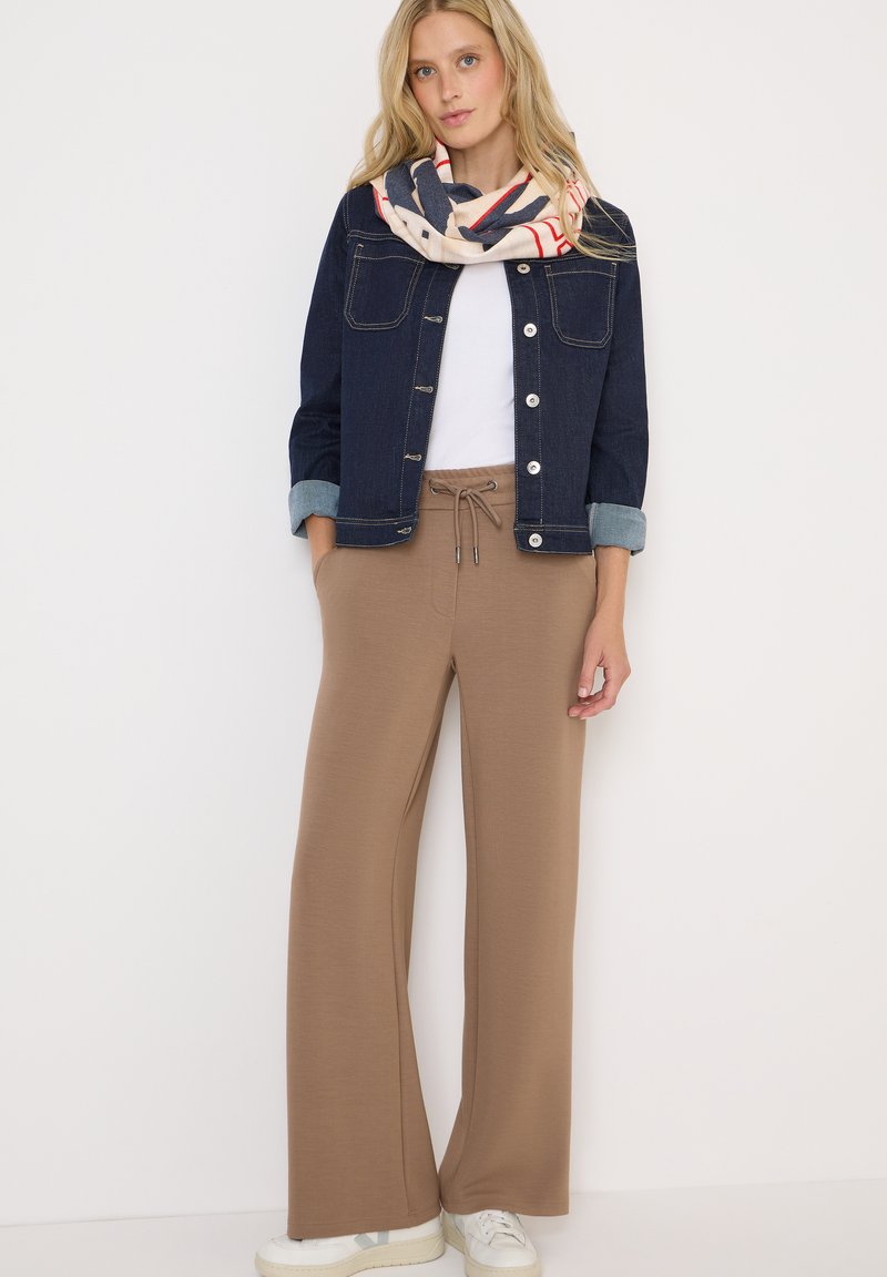 Pantaloni larghi marroni con cordoncino elastico, abbinati a una t-shirt bianca e a un giubbotto in denim scuro. Accessoriati con una sciarpa a fantasia.