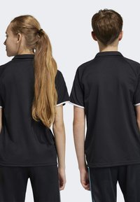 Zwarte sportieve poloshirts met witte accenten, met een klassieke kraag en korte mouwen, te zien op twee personen van achteren.