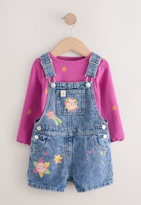 Petos vaqueros con parches coloridos de estrellas y soles, combinados con una camiseta de manga larga rosa acanalada. Cuenta con tirantes ajustables y botones a presión.