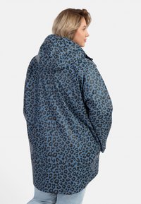 Blå leopardmönstrad hoodiejacka med lös passform och mjuk textur. Har svarta leopardfläckar och en längre baksilhuett.
