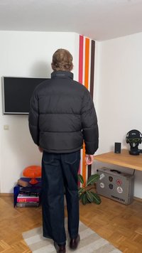 Fekete puffert dzseki magas gallérral és vastag töltelékkel. Cipzárral rendelkezik, bő sötét farmernadrággal és barna cipővel viselik.