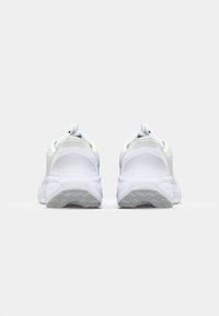 White athletic sneakers with textured mesh panels, rounded heels, rubber soles, and a pull tab at the back for easy wear.