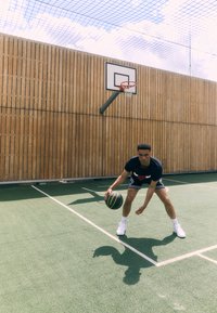 Basketball court scene featuring a player in a black t-shirt and black shorts, dribbling a yellow and black basketball on green flooring.