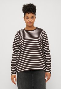 Camisa de rayas marrón y blanca de manga larga con cuello redondo y ajuste holgado, combinada con una falda de mezclilla oscura. Textura de tela suave.