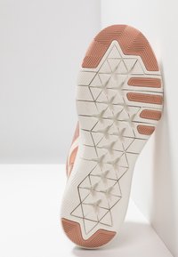 Zool van een schoen met roze accenten, voorzien van een gestructureerde witte rubberen onderkant. Het ontwerp bevat geometrische patronen en grip-elementen.