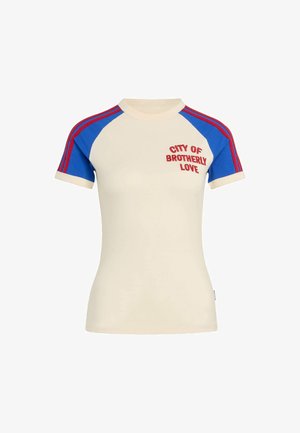 T-shirt court crème à manches courtes avec manches raglan bleues, rayures rouges sur les épaules et texte rouge « City of Brotherly Love » sur la poitrine.