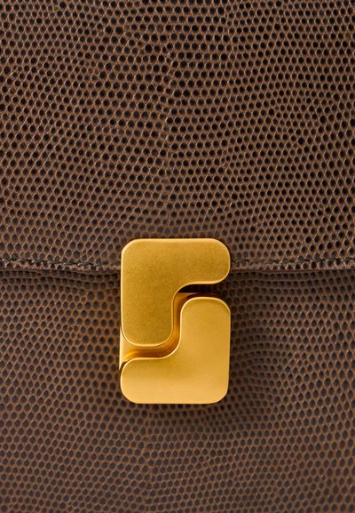 Gros plan sur un cuir texturé marron foncé avec un fermoir géométrique doré sur un rabat de sac ou de pochette.