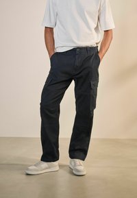 Pantalones cargo en color azul marino con múltiples bolsillos, diseño de pierna recta y un corte relajado, combinados con zapatillas blancas y una camiseta de manga corta.