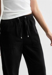 Zwarte broek met een relaxte pasvorm, voorzien van een elastische tailleband en een trekkoord, zijzakken en een gestructureerd katoenen materiaal.