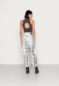 Top curto cinza com texturização e um grande corte circular nas costas, combinado com jeans brancos de algodão com um padrão em tie-dye preto e cinza.