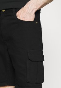 Černé cargo šortky vyrobené z bavlny, s boční kapsou se klopou, knoflíkem v zlaté barvě a rovnou siluetou. Hladká textura a odolná tkanina.