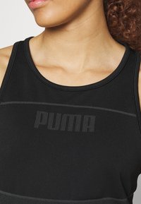 Gros plan d'une personne portant un haut sans manches noir Puma, montrant l'encolure et le haut de la poitrine avec un logo de marque subtilement texturé.