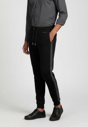 Black jogger pants with a tapered design, featuring side pockets and a reflective stripe. Worn with a gray button-up shirt and black sneakers.