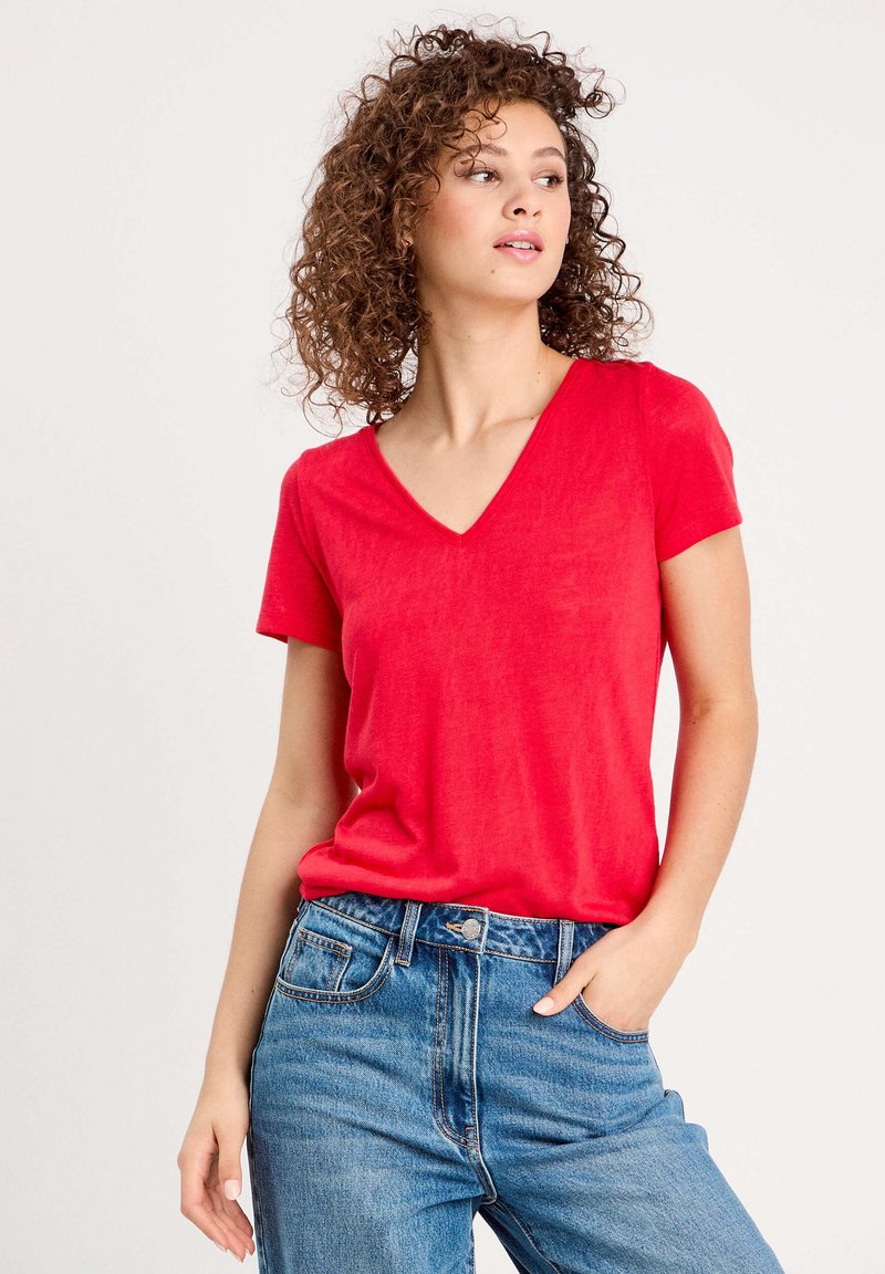 Rotes Baumwoll-T-Shirt mit V-Ausschnitt, kurzen Ärmeln, weicher Textur und entspanntem Schnitt, kombiniert mit hochtaillierten blauen Jeans.