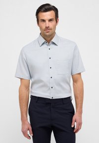 Camicia a maniche corte, a scacchi blu chiaro, con colletto button-down e taschino sul petto, abbinata a pantaloni navy scuri.