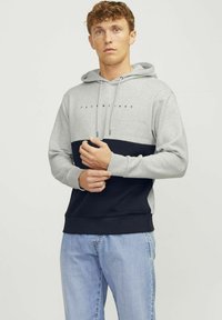 Sudadera color bloque gris y marino con cordón, fabricada en suave algodón, puños acanalados y logo en el pecho; combinada con jeans de color azul claro.