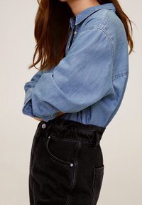 Chemise en denim bleu clair avec une fermeture à boutons à l'avant et des manches retroussées, assortie à un pantalon en denim noir taille haute au fit décontracté.