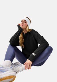 Felpa nera con polsini a costine, abbinata a leggings blu. Una fascia bianca per la testa e sneaker chiare con accenti pastello completano l'outfit.