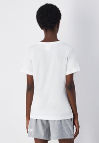 T-shirt bianco a maniche corte con un ampio scollo e cuciture piatte, realizzato in tessuto morbido. La vista posteriore mostra una vestibilità rilassata e nessun logo visibile.