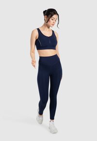 Marineblauwe sport-bh met een ritssluiting aan de voorkant en brede bandjes, gecombineerd met hoog-rise marineblauwe leggings, beide gemaakt van een zachte, rekbare stof.
