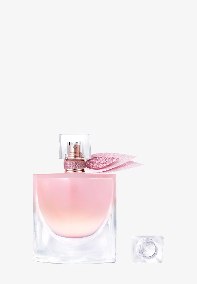 Parfymflaska med rosa gradient och en klar fyrkantig kork, guldaccenter och ett glittrigt rosa band. En liten klar flaska i närheten.