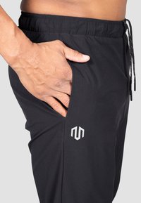 Schwarze Sporthosen verfügen über einen elastischen Bund, eine Seitentasche und ein silbernes Logo am unteren Bein, hergestellt aus leichtem, flexiblem Material.