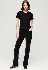 Maglietta nera a maniche corte abbinata a pantaloni neri a campana, entrambi in tessuto uniforme. Le scarpe sono stivali neri a punta.