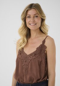 Débardeur marron avec des détails en dentelle au niveau du décolleté en V et des bretelles. Fabriqué à partir d'un tissu lisse avec une coupe décontractée.