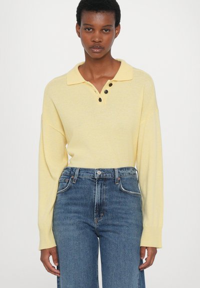 Geltona ilgomis rankovėmis polo marškinėliai su apykakle ir trimis sagutėmis, derinami su aukšto liemens mėlynais džinsais. Minkšta tekstūra ir laisvas kirpimas.