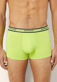 Neon žluté boxerky s černým značkovým pasem. Vyrobeny z měkké tkaniny, mají příjemný střih a střední délku.