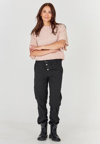 Gaiši rozā īss piedurkņu tops ar brīvu piegriezumu, kombinēts ar piegulošām melnām biksēm, kurām ir divi priekšējie pogas un teksturēta auduma. Melni kaujas zābaki.