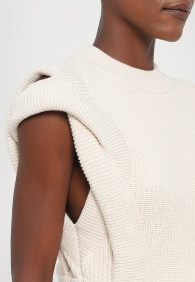 Knit sleeveless top in beige with a high neckline. Features textured fabric, a relaxed fit, and distinctive folded shoulder detail.