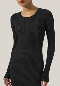 Vestito in maglia a coste nera con maniche lunghe e scollatura a girocollo. La texture è liscia e presenta linee verticali per una silhouette aderente.