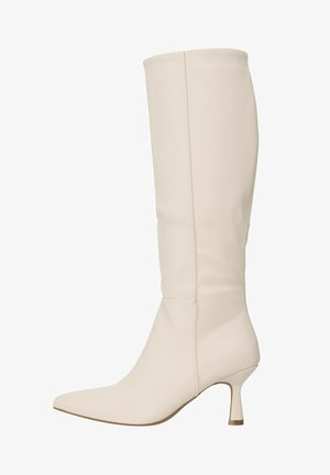 Botte en cuir crème montant jusqu'au genou avec bout pointu et talon moyen fin, vue de profil sur un fond uni.