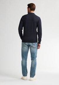 Marineblauwe lange mouwen gebreide top, ronde halslijn, gecombineerd met lichtblauwe spijkerbroek en witte sneakers. Minimalistische stijl, geen zichtbare patronen of accenten.