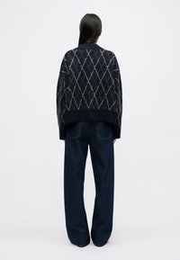 Pull en maille bleu marine avec motif en losange, coupe oversize et poignets côtelés, associé à un jean en denim noir taille haute et ample.