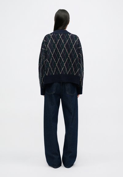 Suéter de punto azul marino con patrón de diamantes, corte oversize y puños acanalados, combinado con jeans oscuro de mezclilla anchos y de tiro alto.