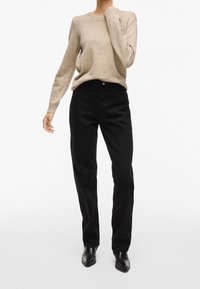 Beige stickad tröja med långärmar, kombinerad med högmidjade svarta byxor. Svarta läderstövlar fullbordar outfiten. Enkelt design och texturer.